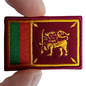 May include: A rectangular embroidered patch featuring the national flag of Sri Lanka. The design includes a vertical green stripe, a vertical orange stripe, and a larger maroon field with a gold lion holding a sword, all bordered in gold.