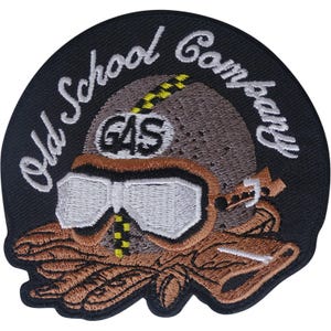 Puede incluir: Un parche bordado circular con fondo negro que presenta el texto Old School Company en letra cursiva blanca. El diseño incluye un casco marrón con gafas blancas, una franja a cuadros amarilla y negra y la palabra GAS en letras negras.