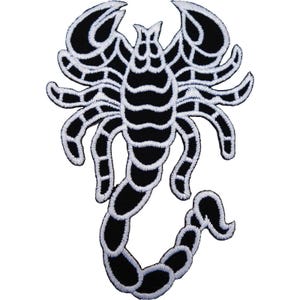 May include: An embroidered patch featuring a stylised scorpion design in black and white. The scorpion is depicted with large pincers, eight legs, and a segmented tail that curves to the right, all outlined in thick white thread.