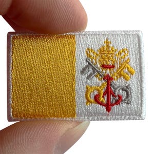 May include: A rectangular embroidered patch featuring the flag of Vatican City. The left side is solid yellow, while the right side is white and displays the crossed keys of Saint Peter in yellow and silver, topped by a red papal tiara.