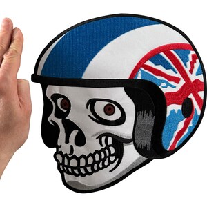 May include: An embroidered patch featuring a white skull wearing a motorcycle helmet. The helmet is white with a blue stripe and a red, white, and blue Union Jack flag design on the side. The skull has black outlines and red-tinted eye sockets.