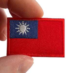 May include: A rectangular embroidered patch featuring the flag of Taiwan. The design consists of a solid red field with a blue canton in the upper left corner, containing a white sun with twelve triangular rays radiating from a central circle.