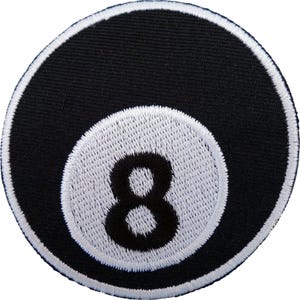 May include: A circular embroidered patch featuring a black background with a white border. In the centre, a white circle contains a black number eight. The design mimics the appearance of a classic eight ball from a game of billiards.
