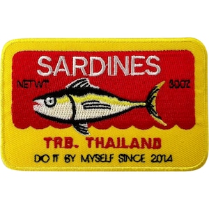 May include: A rectangular embroidered patch with a yellow border and a red center. It features a white fish illustration, the text SARDINES, NET WT 3OZ, TRB. THAILAND, and DO IT BY MYSELF SINCE 2014 in black and white thread on a fabric background.