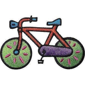 May include: An embroidered patch shaped like a bicycle with an orange frame, a blue seat, and a blue headlight. The wheels are green with pink spokes and black outlines. A purple chain guard covers the centre, and a small black pedal is visible.