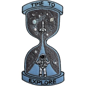 May include: An embroidered patch shaped like an hourglass with light blue borders and text that reads TIME TO EXPLORE. The top bulb features a white space shuttle against a dark grey starry background, while the bottom bulb contains an astronaut.