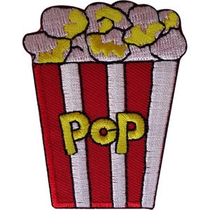 Puede incluir: Un parche bordado con forma de cubo de palomitas de maíz con rayas verticales rojas y blancas. La parte superior presenta granos de palomitas blancos y amarillos. La palabra POP está bordada en letras amarillas grandes en el centro del cubo.