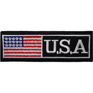 Op de afbeelding: Een rechthoekige geborduurde patch met een zwarte achtergrond en een witte rand. Links een gestileerde Amerikaanse vlag met rode en witte strepen en een blauw kanton met witte sterren. Rechts de witte tekst U.S.A in een schreeflettertype.