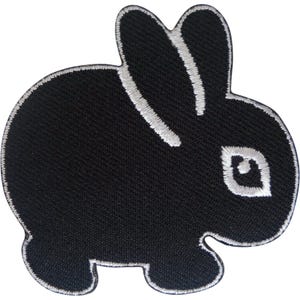 May include: A black embroidered patch in the shape of a small rabbit. The rabbit is depicted in profile facing right, featuring white thread detailing along the ears, the outline of the body, and a small white eye with a black centre.