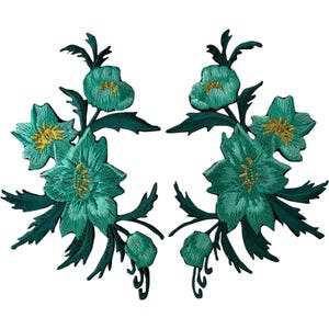 May include: Two symmetrical floral embroidered patches featuring teal and dark green petals with metallic gold thread accents in the centres. Each patch displays a cluster of blooming flowers and pointed leaves arranged in a vertical spray.