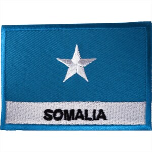 May include: A rectangular embroidered patch featuring a medium blue background with a centered white five-pointed star. A horizontal white stripe runs across the lower portion of the patch, containing the black embroidered text SOMALIA.
