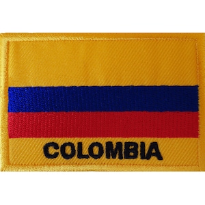 Puede incluir: Un parche rectangular bordado que presenta la bandera tricolor horizontal de Colombia con una franja superior amarilla ancha, una franja central azul y una franja inferior roja. La palabra COLOMBIA está bordada en letras negras mayúsculas.