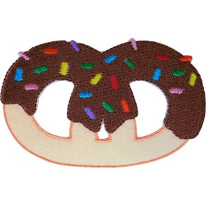 Op de afbeelding: Een geborduurde patch in de vorm van een krakeling, met een lichtbruine deegbasis en een donkerbruin, chocoladekleurig bovengedeelte. Het chocoladegedeelte is versierd met kleine, veelkleurige geborduurde spikkels in blauw, groen, rood, geel en roze.