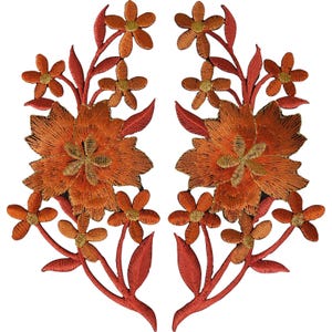 Può includere: Due toppe ricamate simmetriche raffiguranti grandi fiori centrali arancioni con centri dorati, circondati da fiori più piccoli e foglie sottili. L'intricata lavorazione a filo crea un motivo floreale strutturato nei toni dell'arancio bruciato e dell'oro.