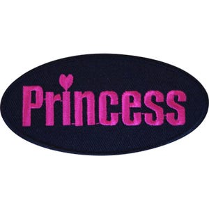 Puede incluir: Un parche bordado de forma ovalada con un fondo azul marino oscuro. La palabra Princess está bordada con hilo rosa brillante en el centro, con un pequeño icono de corazón rosa que reemplaza el punto sobre la letra i en la palabra.