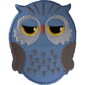 May include: An embroidered patch shaped like an owl with a light blue body, dark gray wings, and white feathered accents around the eyes. The owl has yellow eyes with black pupils, a small orange beak, and dark gray geometric patterns on its chest.