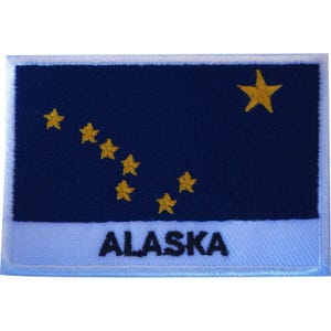 May include: A rectangular embroidered patch featuring the Alaska state flag design. The patch has a dark blue background with eight gold embroidered stars arranged in the Big Dipper and North Star pattern, with the word ALASKA in black text.