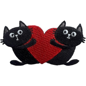 Puede incluir: Un parche bordado que muestra dos gatos negros frente a frente, cada uno con ojos y bigotes blancos, sosteniendo un gran corazón rojo central entre ellos. Los gatos tienen orejas puntiagudas y están representados con hilo negro.