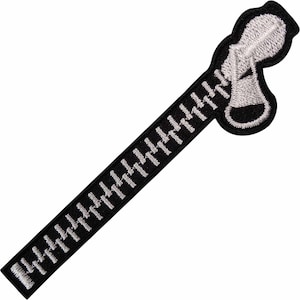 May include: An embroidered iron-on patch featuring a black fabric strip with a white stitched zip design. The patch includes a detailed white zip pull tab at the top, with individual white teeth extending down the length of the black border.