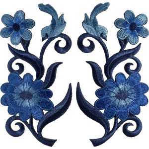 Könnte beinhalten: Zwei symmetrische Stickaufnäher mit einem Blumen- und Vogelmotiv in Blautönen. Jeder Aufnäher zeigt eine große untere Blume, eine kleinere obere Blume, geschwungene dunkelblaue Blätter und einen stilisierten Vogel auf einem Rankenstängel.