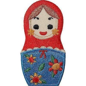 May include: An embroidered patch shaped like a Russian nesting doll. The top section is red with a cream-coloured face, brown hair, and black eyes. The bottom section is blue with a floral pattern featuring red and yellow flowers and green leaves.