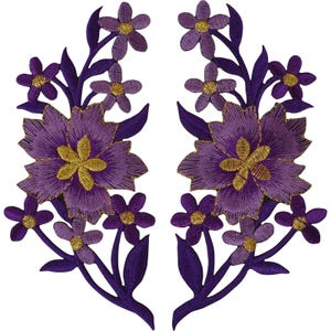 Könnte beinhalten: Ein Paar symmetrische, bestickte Blumenaufnäher mit großen violetten Blüten und goldgelben Mitten, umgeben von kleineren violetten Blüten und dunkelvioletten Blättern. Die aufwendige Stickerei erzeugt ein detailliertes botanisches Design.