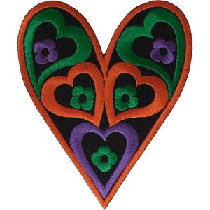 Puede incluir: Un parche bordado en forma de corazón con fondo negro y contornos de corazones entrelazados en naranja, verde y morado. El diseño incluye pequeños motivos florales de cuatro pétalos en colores contrastantes centrados en cada sección.