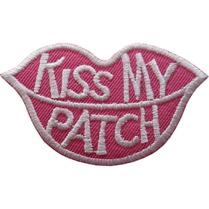 May include: A lip-shaped embroidered patch featuring a vibrant pink background with white stitched borders. The text "KISS MY PATCH" is embroidered in white capital letters across the centre of the lips, creating a bold and clear graphic design.