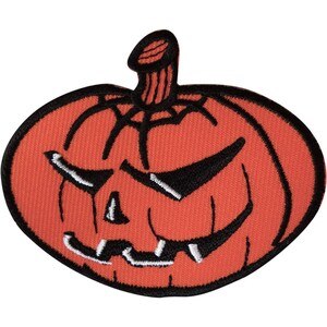 Pode incluir: Um emblema bordado em forma de abóbora com uma superfície laranja brilhante e detalhes em fio preto. A abóbora apresenta um rosto esculpido com olhos afiados e angulares, um pequeno nariz triangular e uma boca serrilhada com dentes.