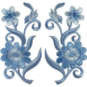 Könnte beinhalten: Zwei symmetrische, hellblaue, bestickte Blumenaufnäher mit einer großen unteren und einer kleineren oberen Blüte, die durch geschwungene Stängel und Blätter verbunden sind. Die komplexe Stickerei zeigt verschiedene Blautöne und verleiht diesen dekorativen Stoffapplikationen eine strukturierte Optik.