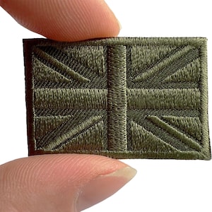 May include: A rectangular embroidered patch featuring a monochromatic olive green Union Jack flag design. The stitching is dense and uniform, creating a textured surface that replicates the iconic British flag pattern in a single muted colour tone.