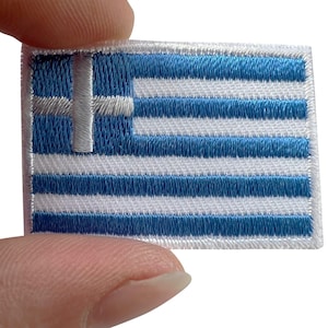 May include: A rectangular embroidered patch featuring the national flag of Greece. The design consists of nine horizontal stripes alternating between blue and white, with a white cross centered on a blue square in the upper left corner.