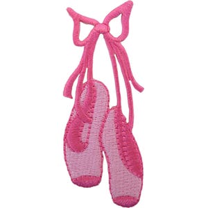 Può includere: Una toppa ricamata rosa raffigurante un paio di scarpette da danza classica legate insieme da lunghi nastri che formano un fiocco in alto. Le scarpette sono realizzate in due tonalità di filo rosa con dettagli di cucitura visibili.
