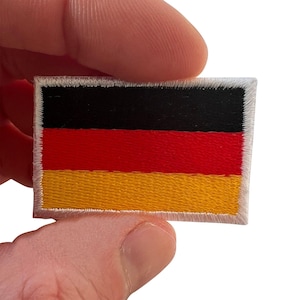 Puede incluir: Un parche rectangular bordado que presenta la bandera tricolor horizontal de Alemania con franjas negra, roja y dorada. El parche tiene un borde blanco cosido alrededor de todo el perímetro, lo que proporciona un acabado limpio al diseño.