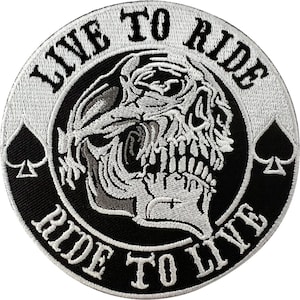 May include: A circular embroidered patch featuring a white skull graphic centred on a black background. The text LIVE TO RIDE is arched across the top, and RIDE TO LIVE is arched across the bottom in white lettering. Two white spade symbols are on the sides.