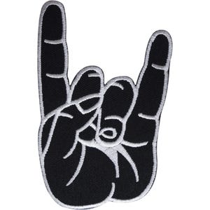 Puede incluir: Un parche bordado negro con la forma de una mano haciendo el signo de rock and roll. El diseño presenta un fondo negro sólido con contornos cosidos en blanco que definen los dedos, los nudillos y la palma, creando una silueta gráfica clara.
