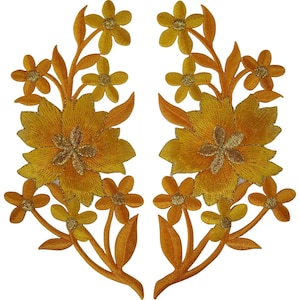 Puede incluir: Un par de parches bordados simétricos con diseños florales en amarillo dorado. Cada parche muestra una flor central grande rodeada de flores más pequeñas y hojas, todo realizado con hilo amarillo vibrante y dorado metálico.