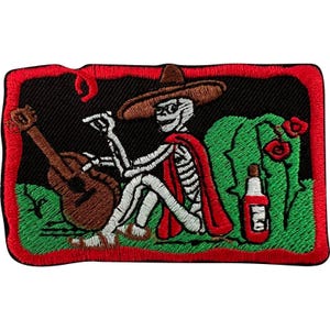 May include: A rectangular embroidered patch featuring a skeleton wearing a brown sombrero and a red cape, sitting on green grass. The skeleton holds a brown acoustic guitar. A red bottle and red flowers are nearby, all bordered by a red frame.