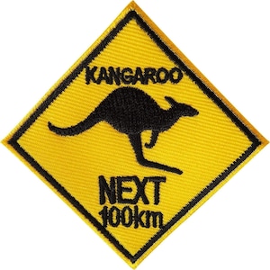 Peut inclure: Un écusson brodé en forme de losange avec un fond jaune et une bordure noire. Il présente une silhouette noire de kangourou au centre, avec le texte noir KANGAROO au-dessus et NEXT 100km en dessous du graphique de l'animal.