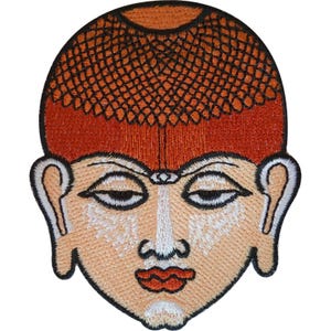 May include: An embroidered patch featuring a stylized human face with a textured, reddish-brown hair pattern, light beige skin, dark outlined eyes, and red lips. The design is enclosed by a thick black border, creating a distinct, flat graphic representation.