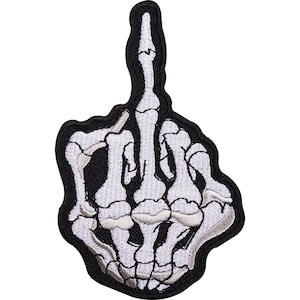 May include: An embroidered patch featuring a white skeleton hand against a black background. The hand is depicted in a gesture with the middle finger extended upward, showing detailed bone structures and joints outlined in black thread.