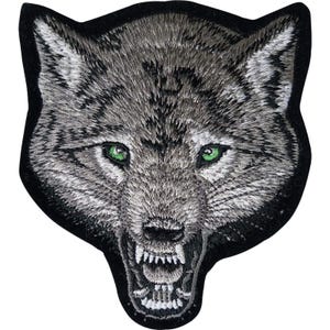 Pode incluir: Um emblema bordado apresentando a cabeça de um lobo com pelo cinza e branco, olhos verdes brilhantes e penetrantes, e uma boca aberta revelando dentes brancos afiados. O design é contornado por uma borda preta espessa de alto contraste.