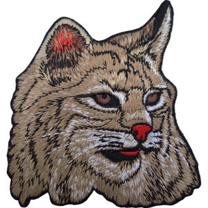 May include: An embroidered patch featuring the head of a bobcat with tan and brown fur, dark brown eyes, a bright red nose, and a red mouth. The design is outlined in black thread, showcasing detailed stitching that mimics the texture of animal fur.