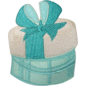 May include: An embroidered patch shaped like a round gift box. The base of the box is a light teal colour with a grid pattern, while the lid is a cream colour. A prominent, textured teal ribbon and bow are stitched across the top of the box.