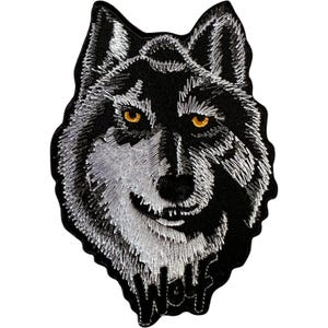 May include: An embroidered patch featuring the head of a wolf with black and white fur detailing. The wolf has piercing amber-coloured eyes and a black nose. The word Wolf is stitched in black thread at the bottom of the patch against a black background.