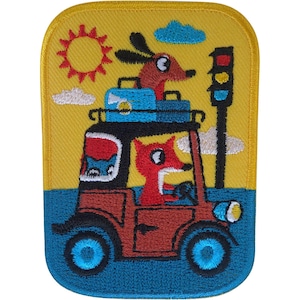 May include: A rectangular embroidered patch featuring a red fox driving a brown car with blue wheels. A brown dog sits on the roof with blue luggage. The scene includes a yellow sun, white clouds, and a black traffic light against a yellow sky.