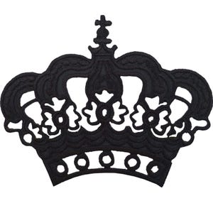 Op de afbeelding: Een zwarte geborduurde patch in de vorm van een kroon. Het ontwerp bevat ingewikkeld stikwerk met een centraal kruis aan de bovenkant, gebogen bogen en een basisband met cirkelvormige uitsparingen. Het borduurwerk heeft een reliëftextuur.