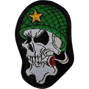 May include: An embroidered patch featuring a white skull wearing a green textured military helmet with a gold star emblem on the front. The skull has a black eye socket and a red and white cigarette in its mouth, all set against a black background.