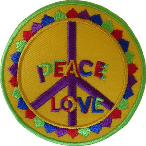 Puede incluir: Un parche bordado circular con fondo amarillo y un símbolo de la paz de color morado. La palabra PEACE está bordada en letras multicolores sobre la palabra LOVE, que también aparece en letras multicolores. Un borde de pequeños triángulos de colores rodea el diseño.