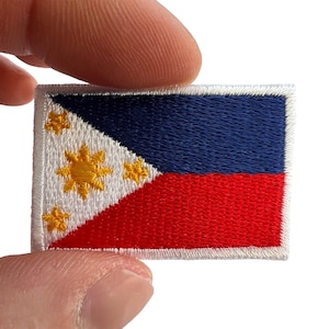 May include: A rectangular embroidered patch featuring the flag of the Philippines. The design includes a white triangle on the left with a central yellow sun and three yellow stars, alongside horizontal blue and red bands with a white border.